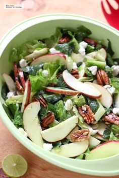 a salad with apples, cheese and pecans in a green bowl on a wooden table