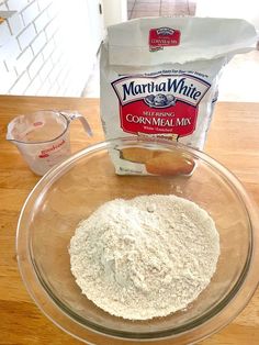 a bowl filled with flour next to a bag of cornmeal mix on top of a wooden table