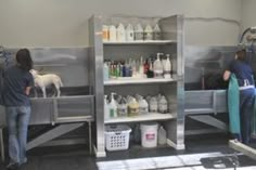 two people in a room with shelves filled with bottles and cleaning supplies on the floor