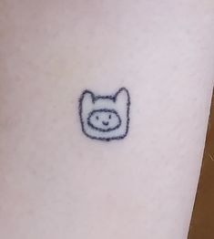 a small tattoo on the leg of a person with a cat face drawn on it