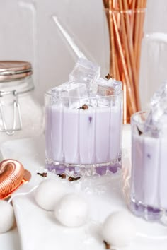 two glasses filled with purple liquid sitting on top of a table next to eggs and cinnamon sticks