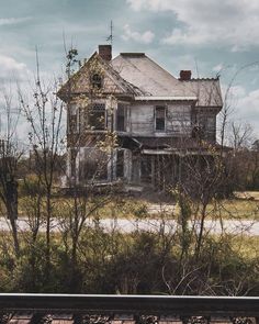 an old abandoned house sitting in the middle of some trees and bushes next to a train track