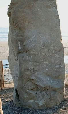 a large rock sitting on top of a sandy beach next to the ocean with writing on it