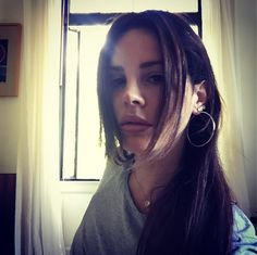 a woman with long brown hair and earrings looking at the camera while standing in front of a window