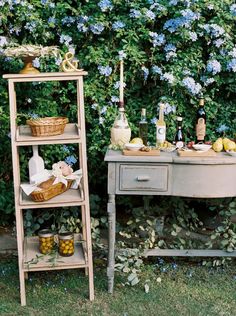 an old wooden table with bottles and baskets on it in front of blue hydranges