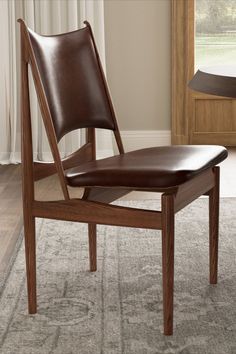 a wooden chair with brown leather upholstered seat and back rests on a carpeted area