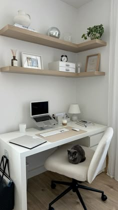 a white desk topped with a laptop computer next to a cat laying on top of it