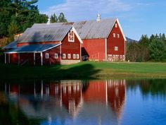 an old red barn is reflected in the water