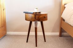 a small wooden table with a book on it next to a bed and a nightstand