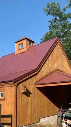 a large wooden barn with a red roof and a tractor parked in front of it