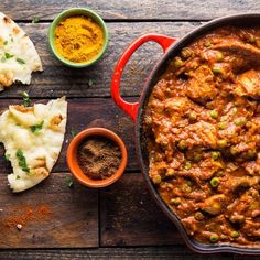 a pan filled with meat and vegetables next to bowls of sauce, bread and spices