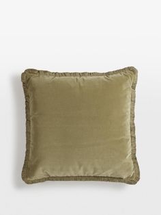 an olive green pillow with ruffled edges on a white wall behind the pillow is a light brown color