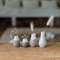 three white vases with flowers in them on a wooden countertop, one is empty and the other two are not