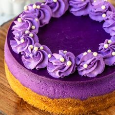 a cake with purple frosting and flowers on it sitting on top of a wooden table