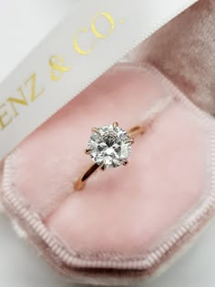 an engagement ring in a pink velvet box with a white ribbon around it and the word enz & co on top