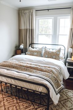 a bed sitting next to a window with curtains on either side and a rug on the floor