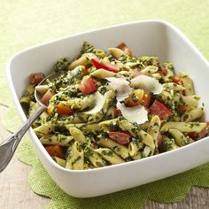 a white bowl filled with pasta and vegetables on top of a green place mat next to a spoon