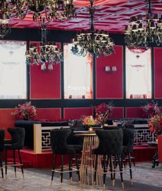 a restaurant with red walls and chandeliers hanging from it's ceiling, surrounded by black velvet chairs