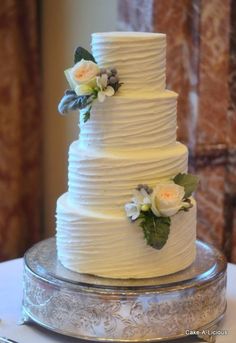 a three tiered white wedding cake with flowers on the top and bottom, sitting on a silver platter