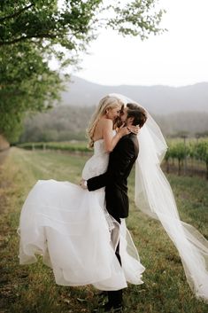 a bride and groom kissing in front of a vineyard at their wedding day, with the veil blowing in the wind