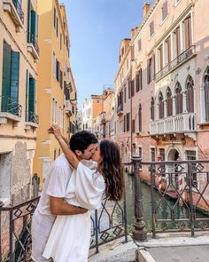 a man and woman are kissing in front of some buildings on the riverwalk, while one holds his arm around the other's neck