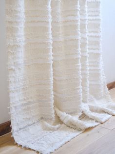 a white curtain with ruffles hanging on the wall next to a wooden floor