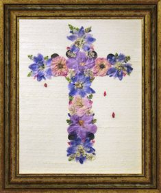 a cross with purple and blue flowers on it in a gold framed frame, hanging on the wall