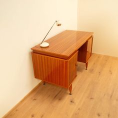 a wooden desk sitting on top of a hard wood floor next to a white wall