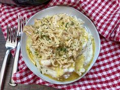 a white plate topped with chicken and pasta next to a fork on a red and white checkered table cloth