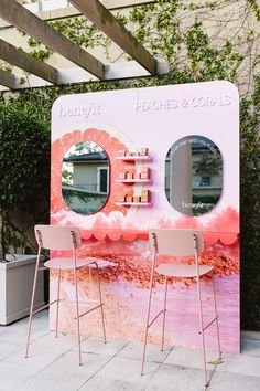 two chairs are sitting in front of a pink booth with mirrors on the wall and plants behind it