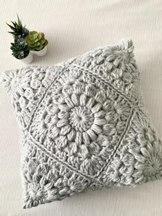 a crocheted pillow sitting on top of a bed next to a potted plant