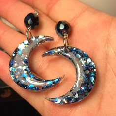 a pair of earrings with blue and silver glitters on them, sitting in someone's hand