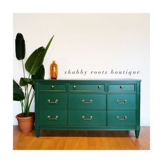 a green dresser sitting on top of a wooden floor next to a potted plant