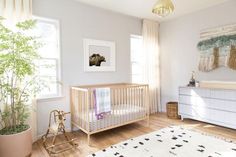 a baby's room with a crib, dresser, and potted plant