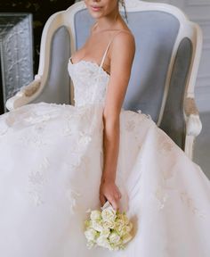 a woman in a wedding dress sitting on a chair holding a bouquet with her hand