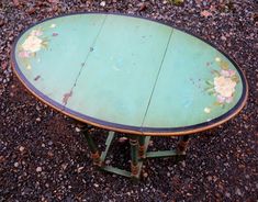 an old table with flowers painted on it sitting in the middle of some gravel ground