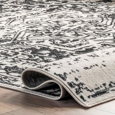 an area rug is laying on the floor in front of a wooden floor with a black and white design