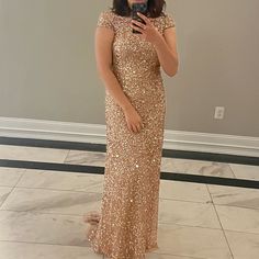 a woman in a gold dress taking a selfie with her cell phone while standing on the floor