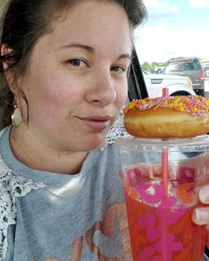 a woman holding up a donut on top of a drink in her hand while sitting in the back seat of a car