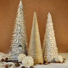 three white christmas trees sitting on top of a table next to pine cones and nuts