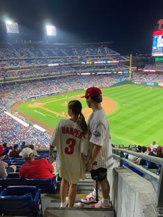 two people standing on the bleachers at a baseball game looking out into the stands