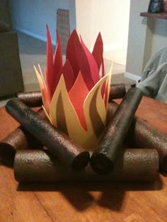 a fire pit made out of rolled up paper on top of a wooden table next to a lamp