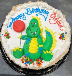 a birthday cake with a green dinosaur holding a red balloon