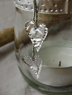 a candle with two hearts hanging from it next to a glass jar filled with candles