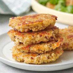 three crab cakes on a white plate next to a bowl of salad and napkins