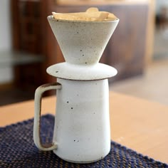 a white coffee pot sitting on top of a wooden table next to a blue place mat