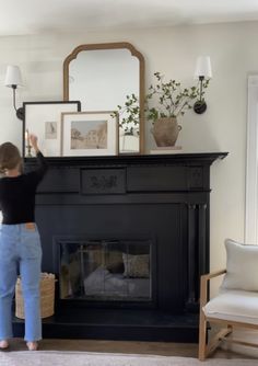 a woman standing in front of a fireplace with a mirror on it's mantle