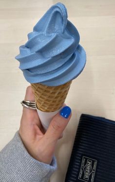 a hand holding an ice cream cone with blue icing on it next to a book