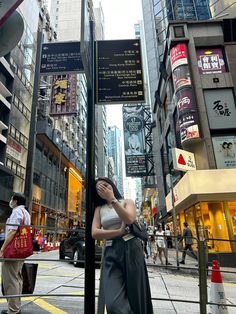 a woman standing on the side of a street next to a pole with signs in it