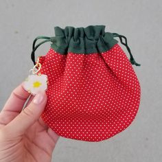 a hand holding a small red bag with white polka dots and a flower on it